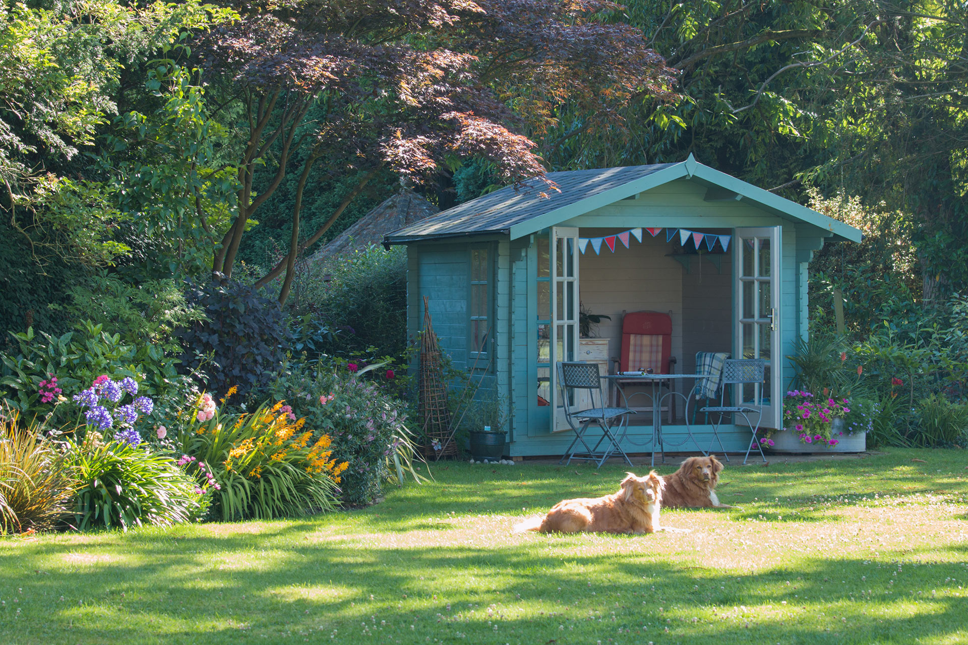 Gemütliches Gartenhaus mit Sitzecke, Hunde liegen auf der Wiese davor, im Garten