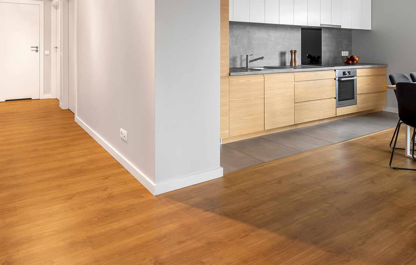 Moderne Küche mit weißer Sockelleiste, Holzoptikboden und grauen Fliesen im Bodenbereich.